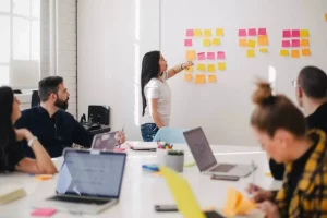 woman at front of meeting using sticky notes on white board